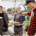 Men of different ages round a BBQ outside