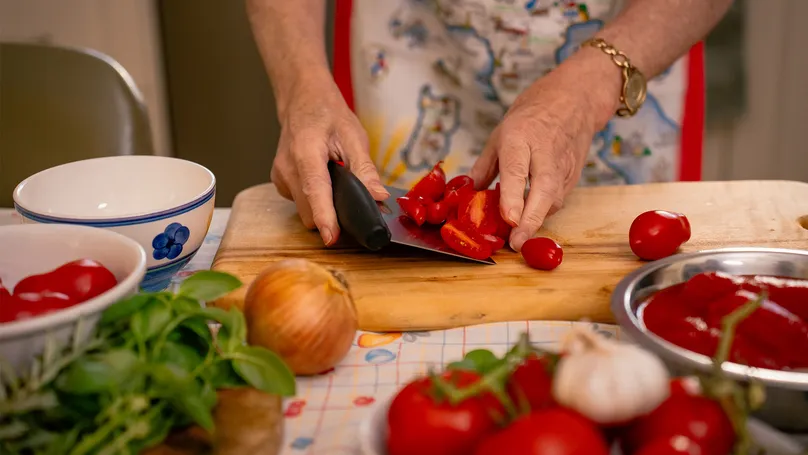 An older woman chops tomatoes with an adaptive grip knife.
