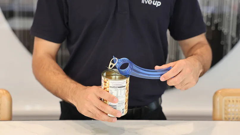 Example of assistive product in use showing a man using an adaptive can opener to open a can