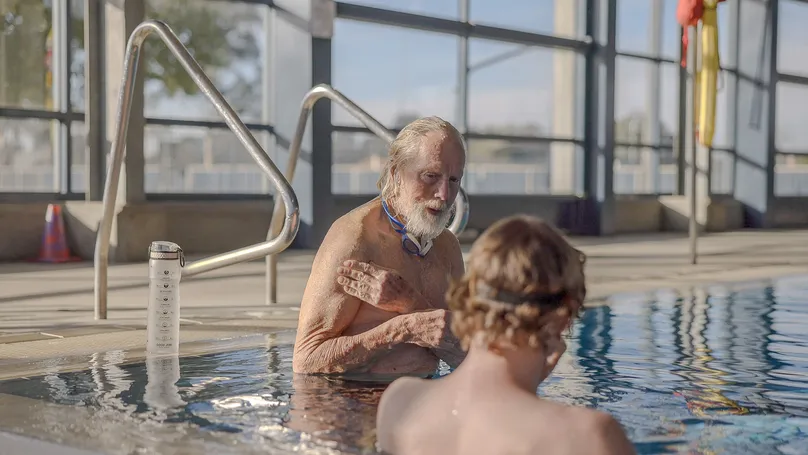 Older man and his son swimming at an indoor pool.