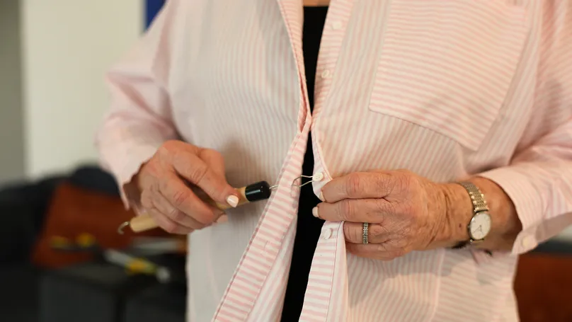 An older woman using a button hook to button up her shirt.