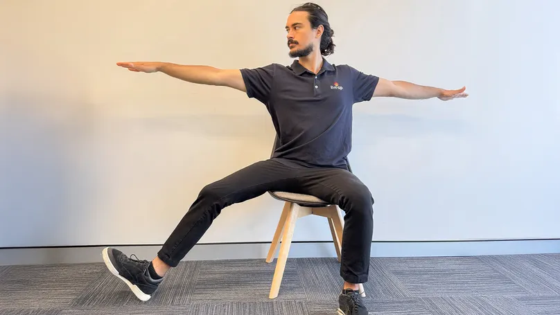 A man doing a seated chair warrior 2 pose.