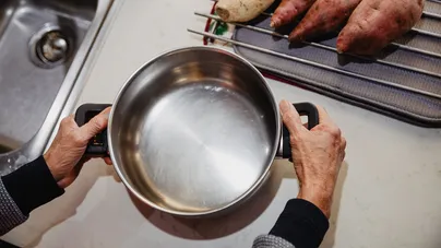 Two hands grasping the handles of a large cooking pot.