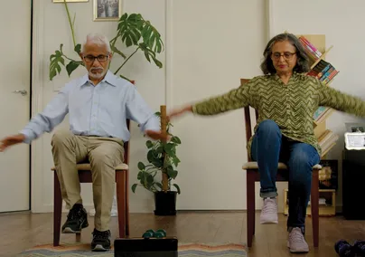 Image of an older couple doing chair exercises in their home.