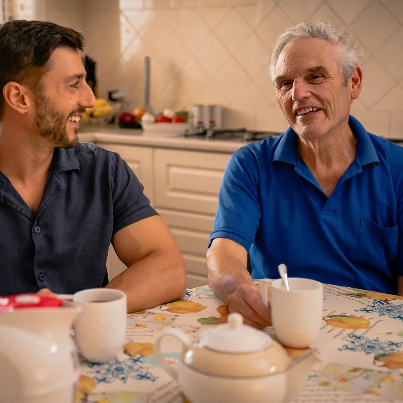A father and son sharing a cup of tea and smiling together.