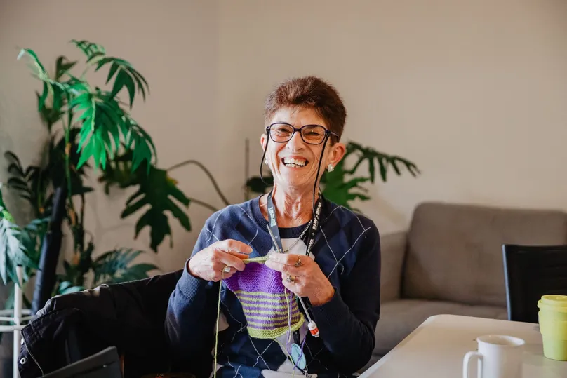 Image of a happy woman knitting on her couch.