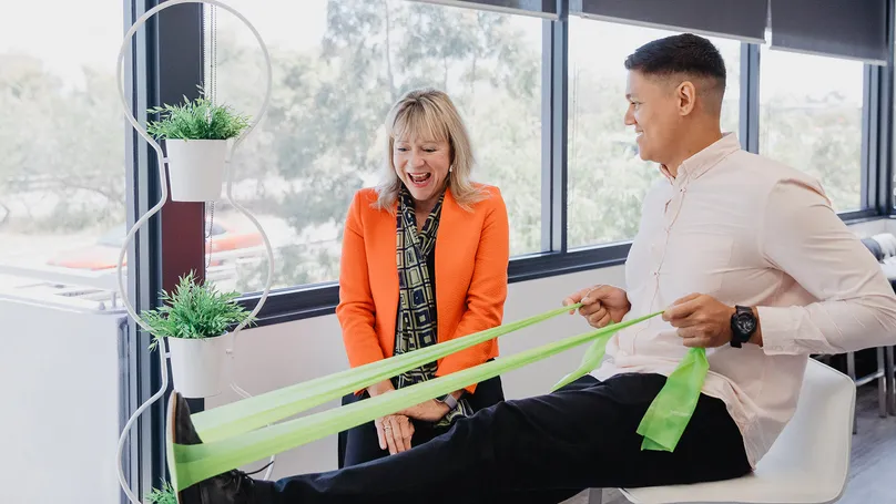 Hilary and Tyler from the LiveUp team laughing together. Tyler is demonstrating use of a resistance band.