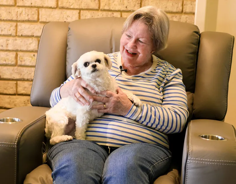 An older woman cuddling with her pet dog on the couch.