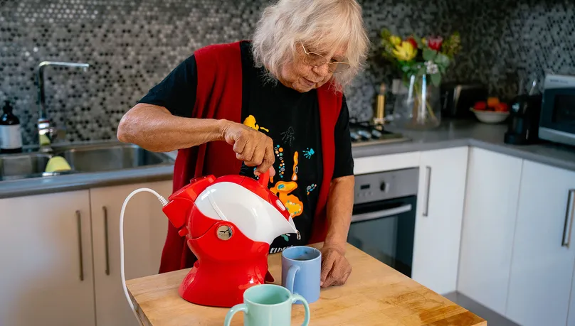 An older woman using a kettle tipper to make tea.