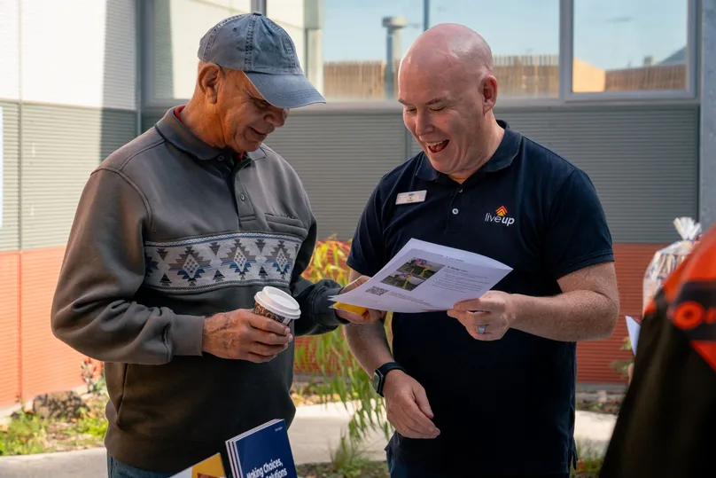 Two men talking over a healthy ageing information sheet at the LiveUp launch.