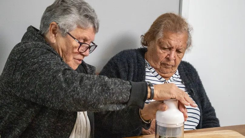 Two older women demonstrating use of an automated food chopper.