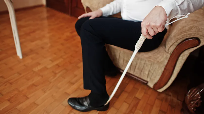 A man using a shoehorn to slide his foot into his shoe.