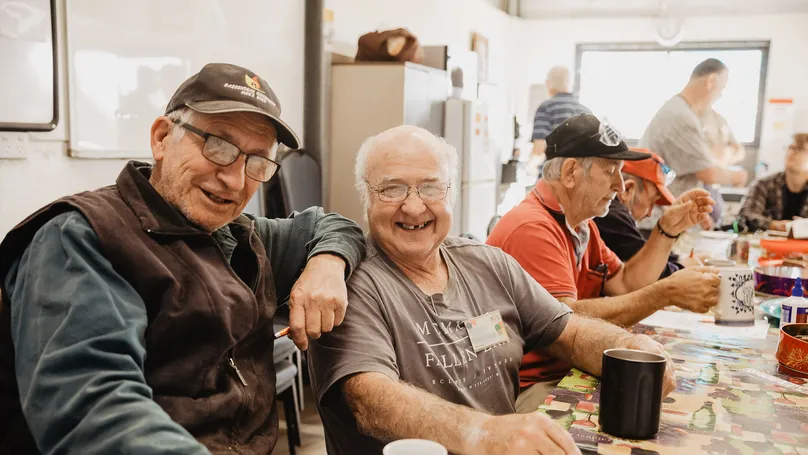 Men sitting together at an event. Two of the men are smiling to the camera.