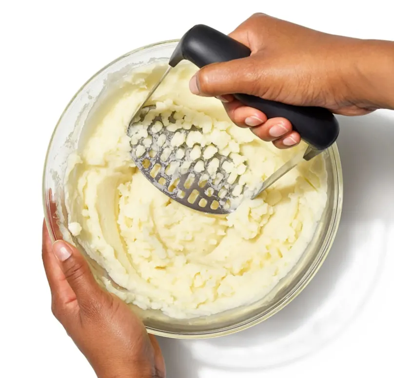 A hand mashing potato in a bowl.