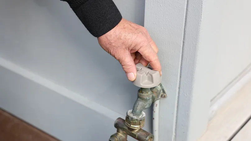 An older man's hand using an outside tap turner to turn on his outdoor tap.