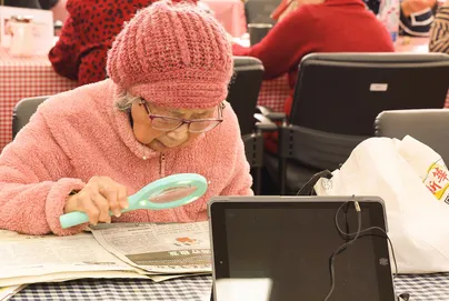 Image of an older woman reading a newspaper with her magnifying glass