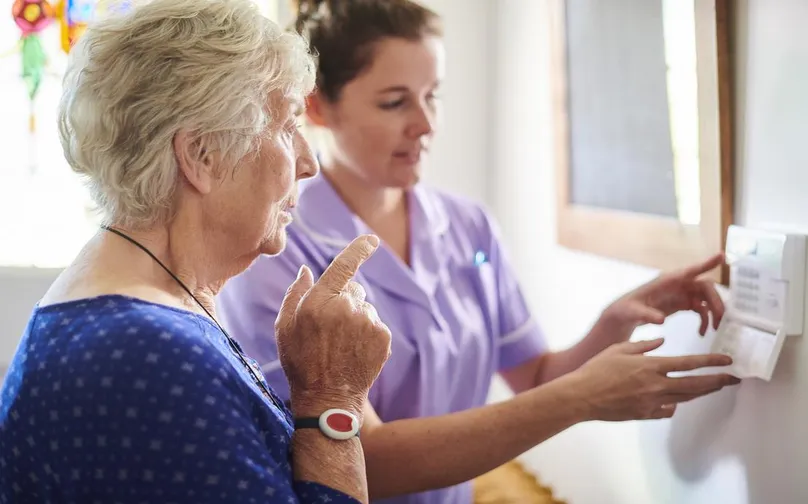 Image of an older woman and nurse installing a personal safety house alarm.