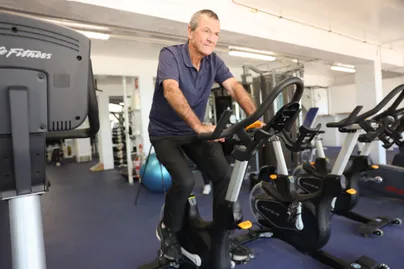 Image of an older man riding on a stationary bike at the gym.