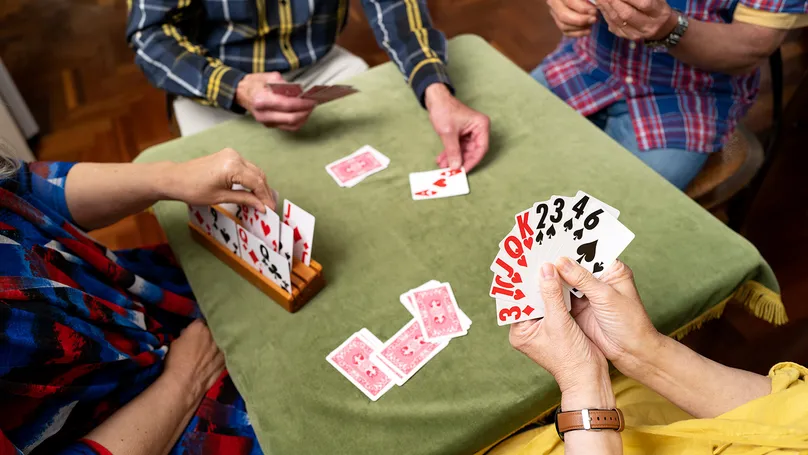 Four people playing card games around a table. They are using cards with big text that are easier to read.