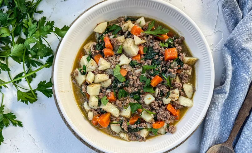A bowl of beef mince stew with diced potatoes, carrots, and chopped parsley.