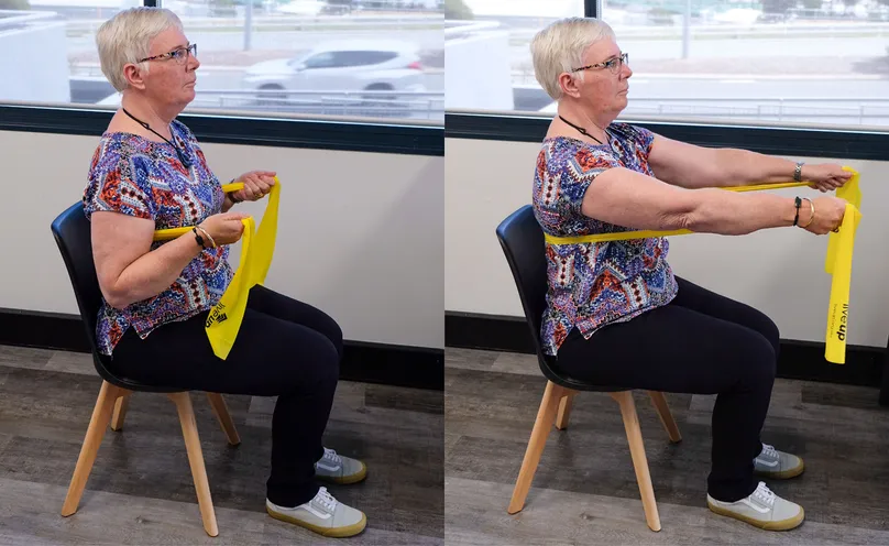 A woman doing a seated chest press with a resistance band.