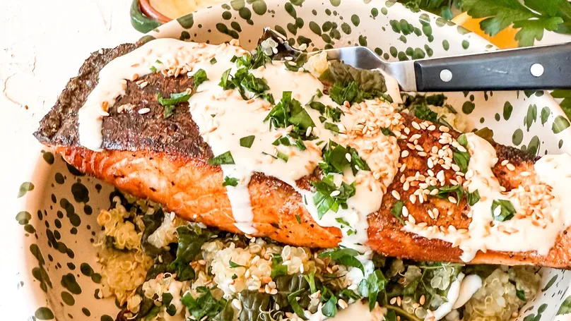 A delicious dish of salmon, kale, and quinoa with tahini drizzled on top.