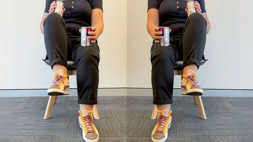 A woman doing seated marching with cans as weights resting on her knees.