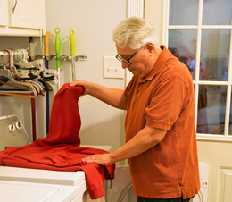 An older person sorting through laundry on top of the washing machine. 
