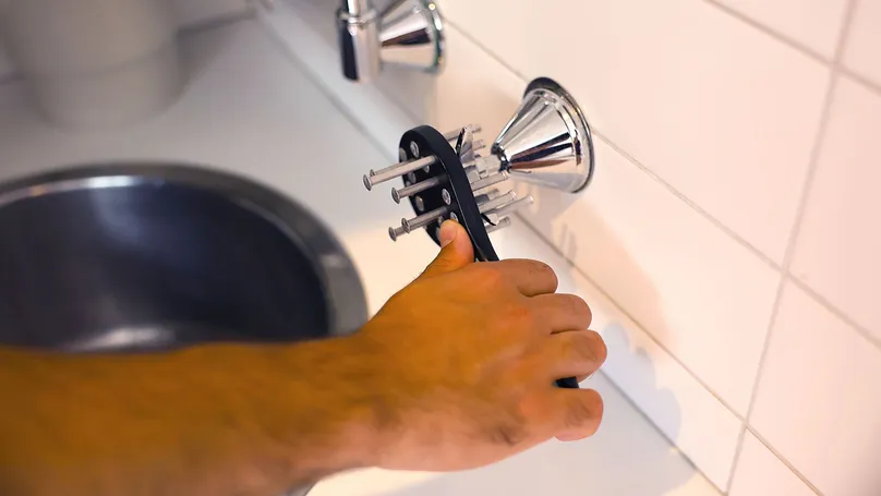 A hand using a tap opener on a bathroom sink valve inside.
