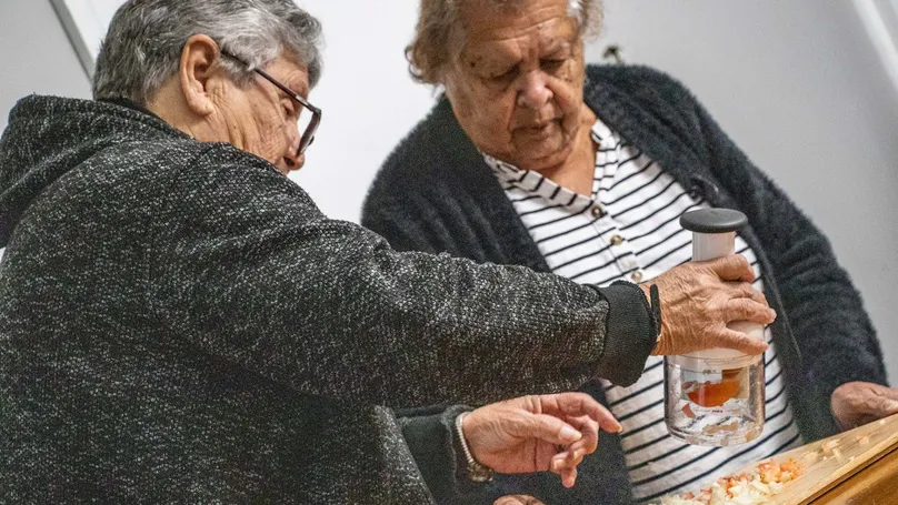 Two older women chopping veggies with a food wand.