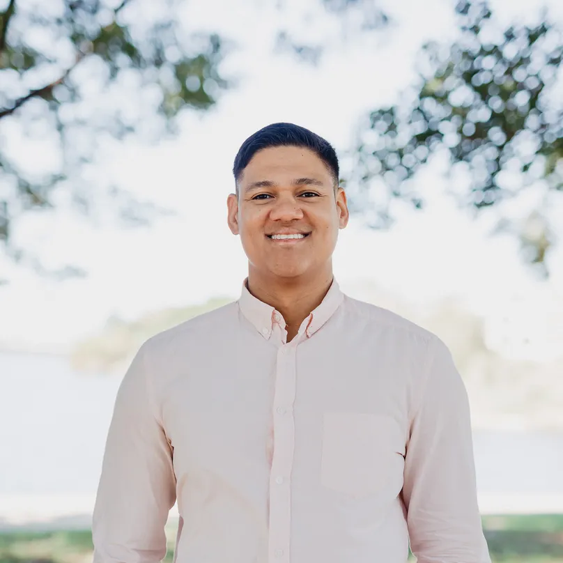 Tyler smiling at the camera, standing in front of a light, natural backdrop.