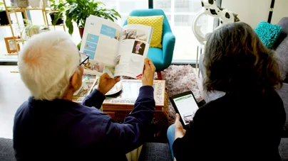 Image of older couple reading booklets and tablets around the coffee table.