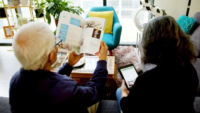 Image of older couple reading booklets and tablets around the coffee table.