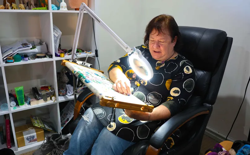 Woman sitting in the chair and doing craft under bright lamp.