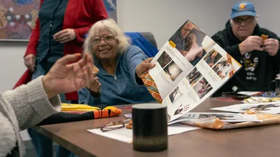 Image of an older woman showing someone a page in a booklet.