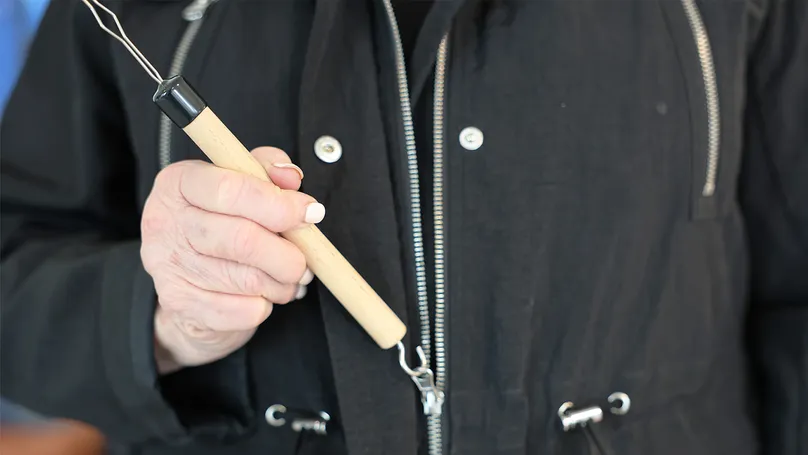 An older woman's hand using a zipper pull to zip up her jacket.