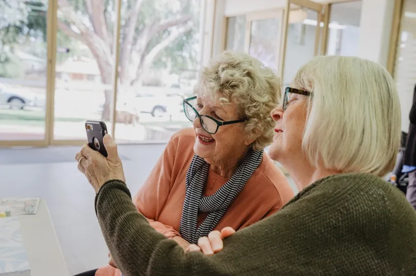 Two ladies sitting, looking at a mobile phone