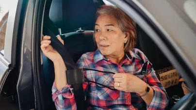 A woman using a seat belt puller to put on her seat belt in a car.
