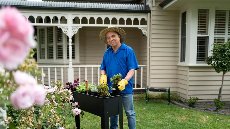 A man gardening outside, standing at his raised garden bed.